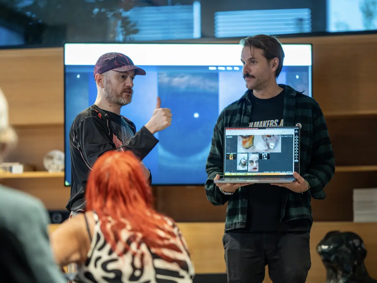 Two filmmakers present their work to the room, one holding up a laptop